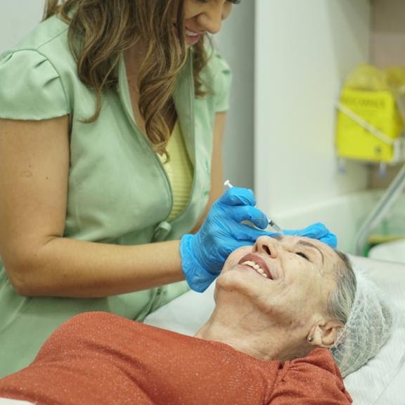 Profissional da DM aplicando um tratamento facial em uma paciente sorrindo